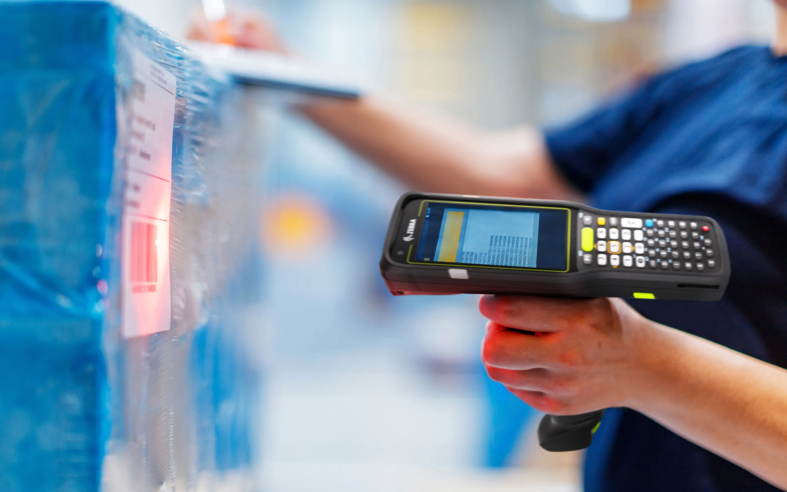 A rugged handheld scanner being used to scan a barcode in a warehouse